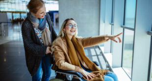 Young disabled woman on wheelchair and carer waiting at airport and looking at window view