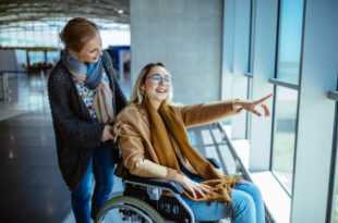 Young disabled woman on wheelchair and carer waiting at airport and looking at window view