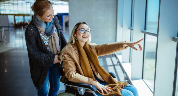 Young disabled woman on wheelchair and carer waiting at airport and looking at window view